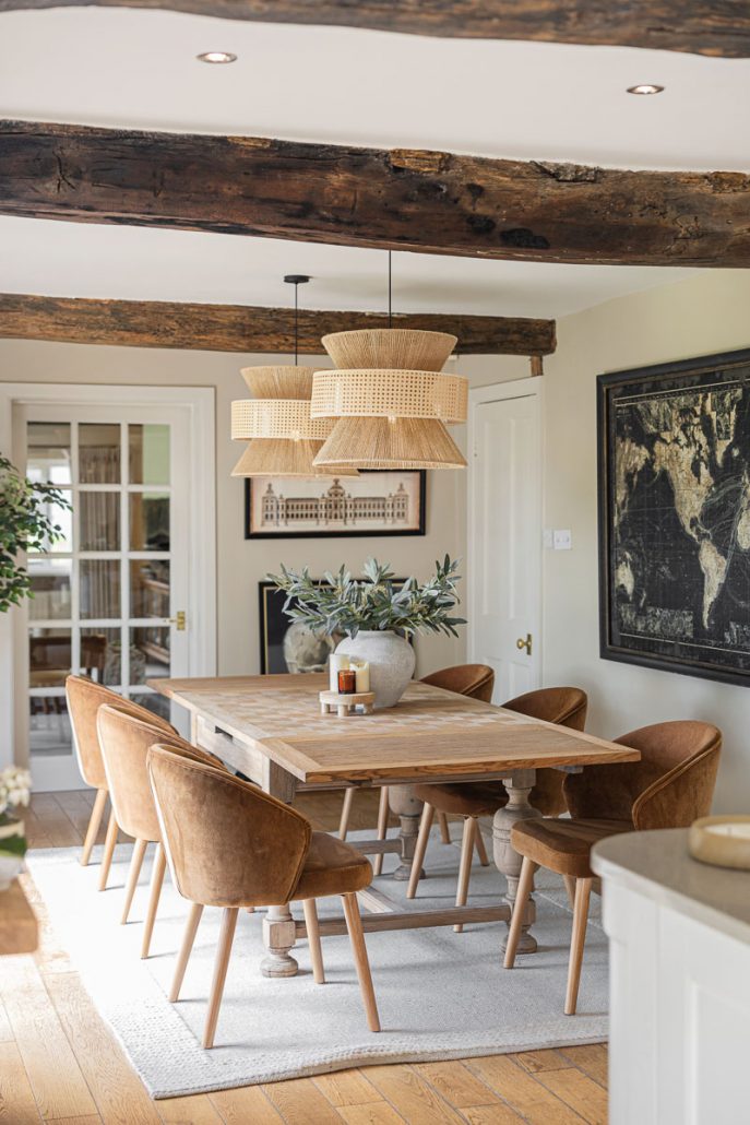 Rustic wooden dining table with velvet chairs and rattan light fittings.