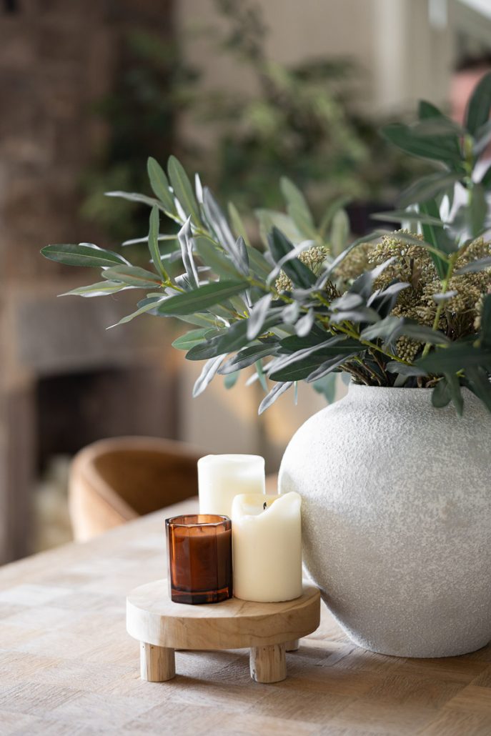 grey vase with greenery and candles on a wooden dining table.