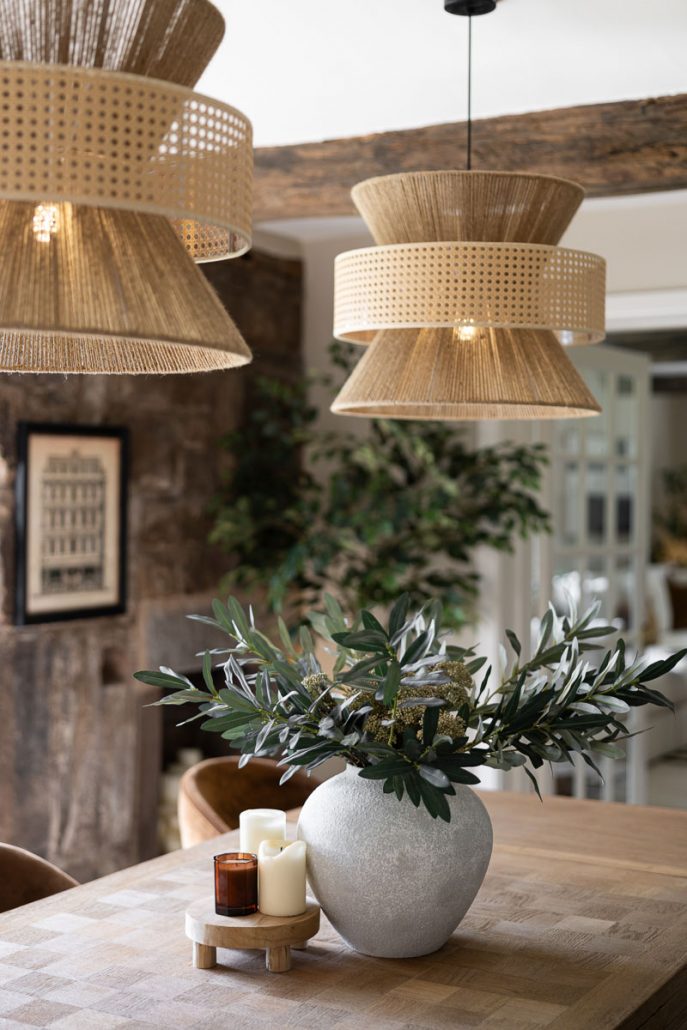 grey vase with greenery and candles on a wooden dining table.