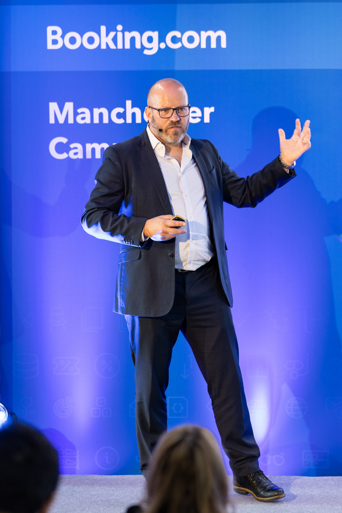 Speaker presenting on stage to a large audience during the Booking.com Elevate corporate event in Manchester
