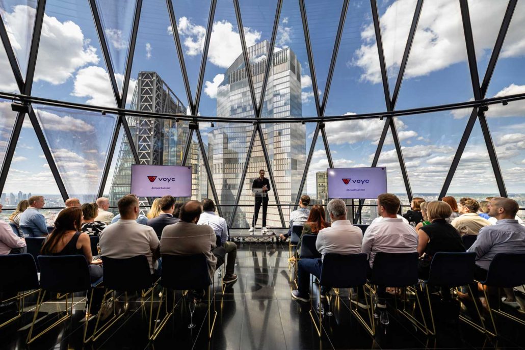 Conference seating and stage inside The Gherkin London with floor-to-ceiling glass overlooking the city skyline