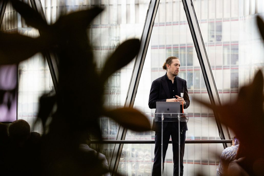 Interior of The Gherkin event space set for a conference, with chairs facing a stage and large windows showing London skyline views including Tower Bridge