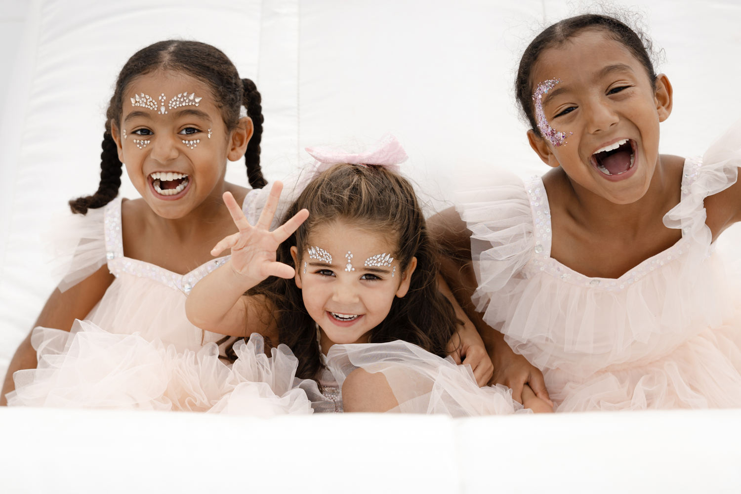 Three young girls in pastel tutu dresses with glitter face paint smiling and posing at a birthday party, captured by a Birthday Party Photographer Manchester